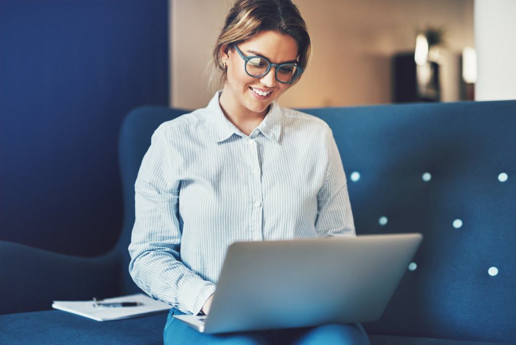 Young female entrepreneur smiling while sitting on a sofa at home workinig online with a laptop